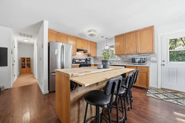 a kitchen with stainless steel appliances a dining table chairs refrigerator and sink
