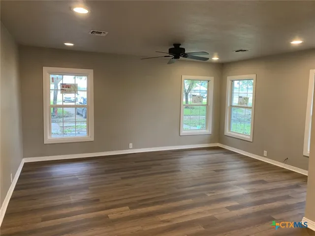 a view of an empty room with wooden floor and a window
