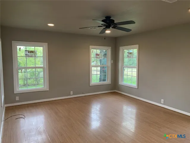 an empty room with wooden floor fan and windows