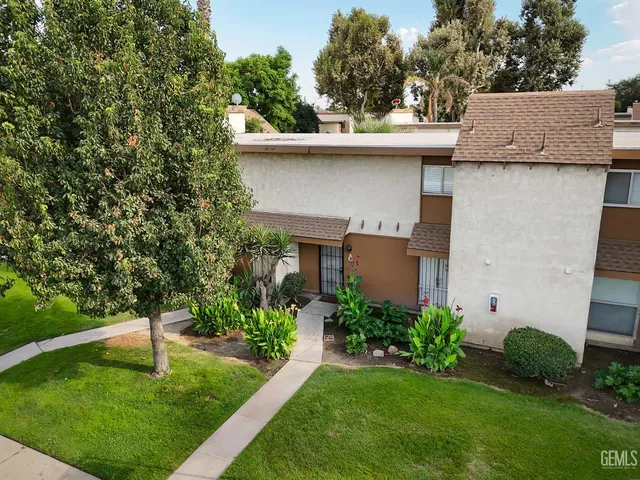 a white house with a small yard plants and a large tree