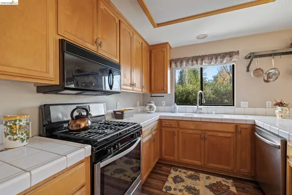 a kitchen with stainless steel appliances granite countertop a refrigerator a sink dishwasher a stove and white countertops with wooden floor