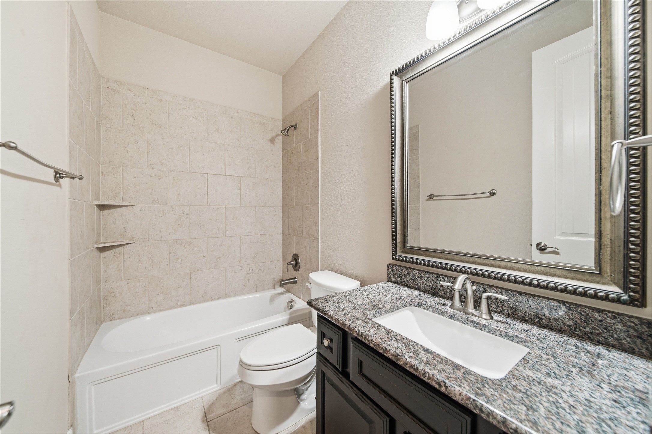 5303 Mesquite Willow Lane Rosharon, TX 77583 - Photo 21 of 32 This secondary bathroom located downstairs features a tiled shower-bathtub combo, a granite countertop with a sink, a large framed mirror, and modern fixtures.