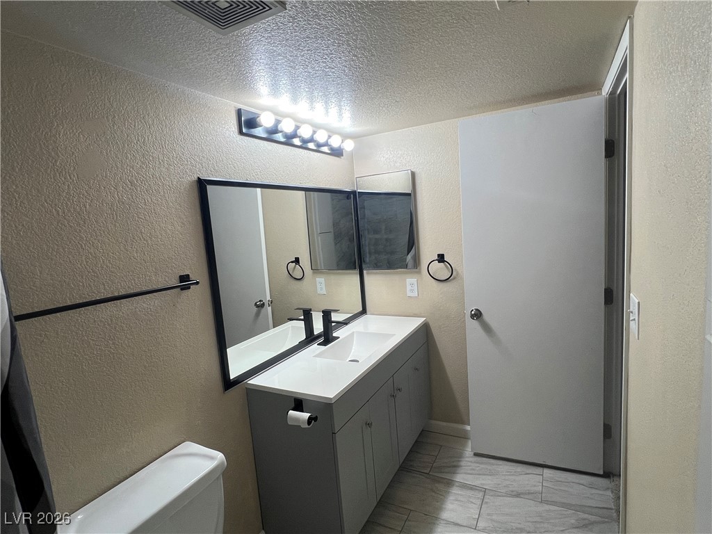 8101 West Flamingo Road, Unit 2161 Las Vegas, NV 89147 - Photo 16 of 21 Half bathroom featuring a textured wall, vanity, light marble finish floors, and a textured ceiling