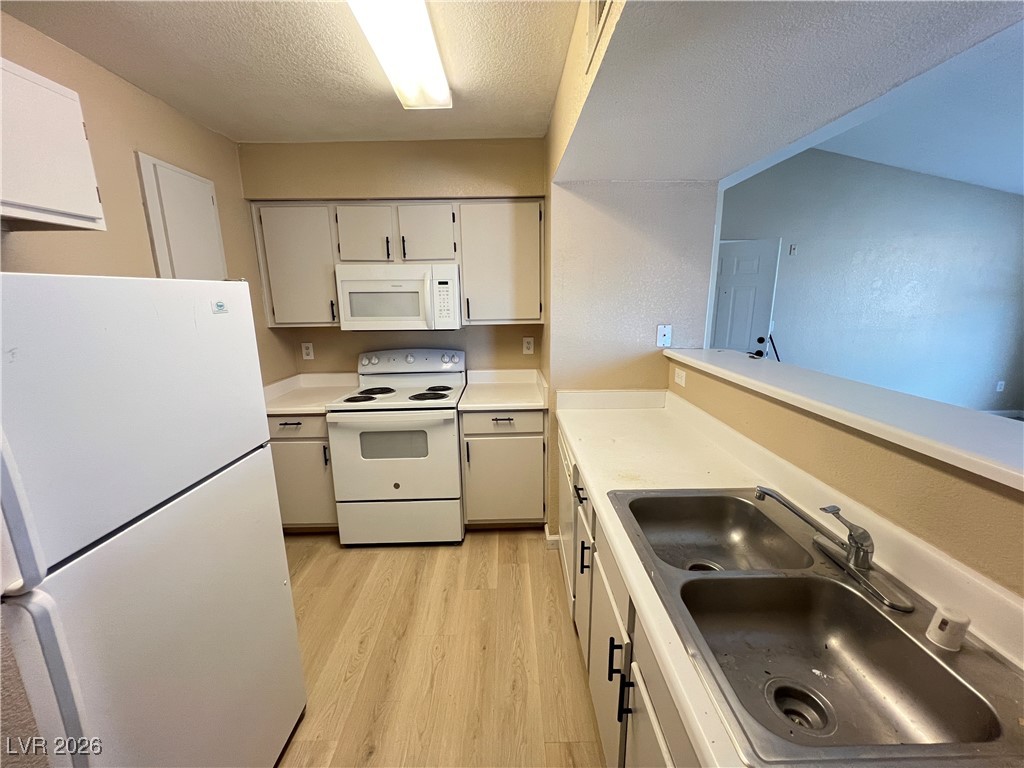 8101 West Flamingo Road, Unit 2161 Las Vegas, NV 89147 - Photo 7 of 21 Kitchen featuring white appliances, a textured ceiling, light countertops, and light wood finished floors