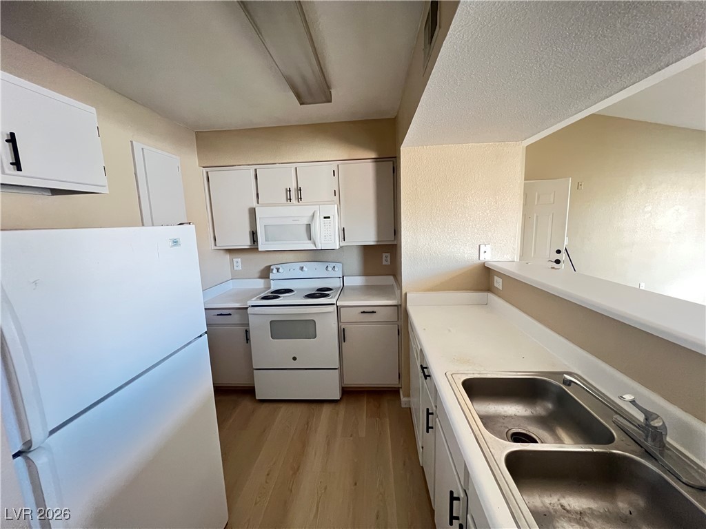 8101 West Flamingo Road, Unit 2161 Las Vegas, NV 89147 - Photo 8 of 21 Kitchen with white appliances, light countertops, light wood-type flooring, white cabinets, and a textured ceiling