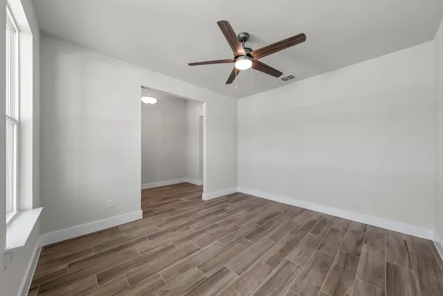 an empty room with wooden floor fan and windows