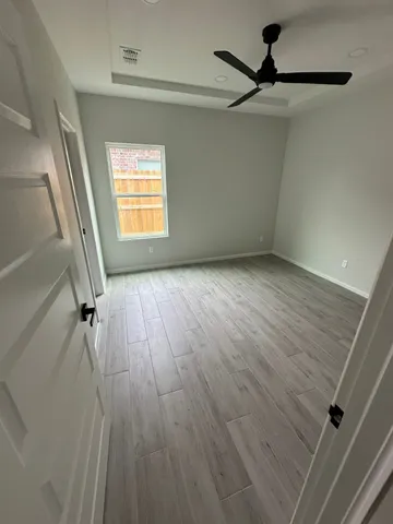 an empty room with wooden floor fan and windows