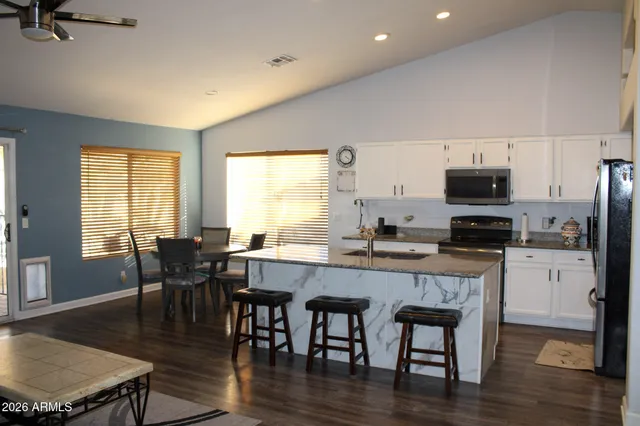 a kitchen with stainless steel appliances granite countertop a stove a refrigerator a microwave a dining table and chairs with wooden floor