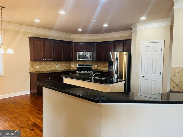 a kitchen with stainless steel appliances granite countertop a refrigerator a stove and a sink with wooden cabinets