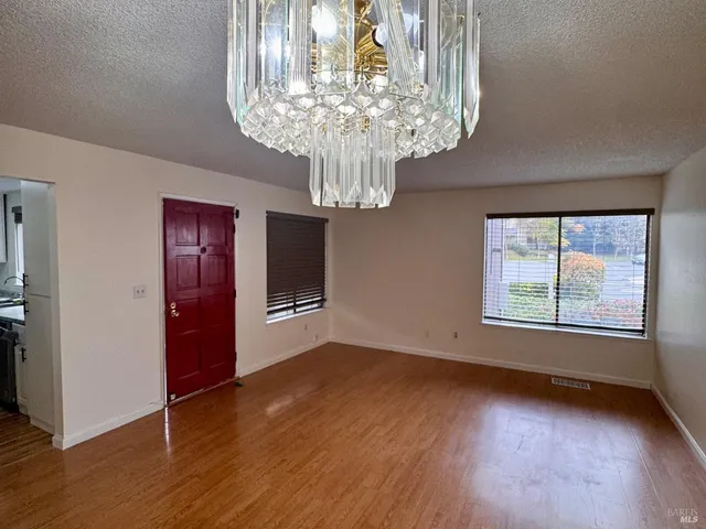 an empty room with wooden floor chandelier and windows