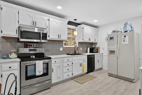 a kitchen with stainless steel appliances granite countertop white cabinets a sink a stove a refrigerator and microwave with wooden floor