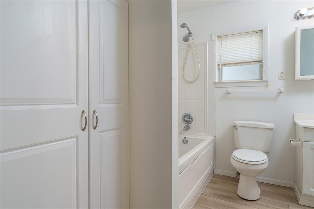 310 North Road Kennedale, TX 76060 - Photo 16 of 23 White paneled storage cabinetry, white bathtub with a shower, white toilet, single vanity with a white countertop, and wood-finish flooring