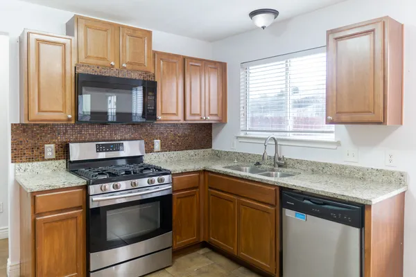 a kitchen with granite countertop a sink stainless steel appliances wooden floor and a window