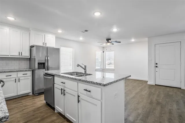 a kitchen with stainless steel appliances granite countertop a sink a stove a refrigerator and white cabinets