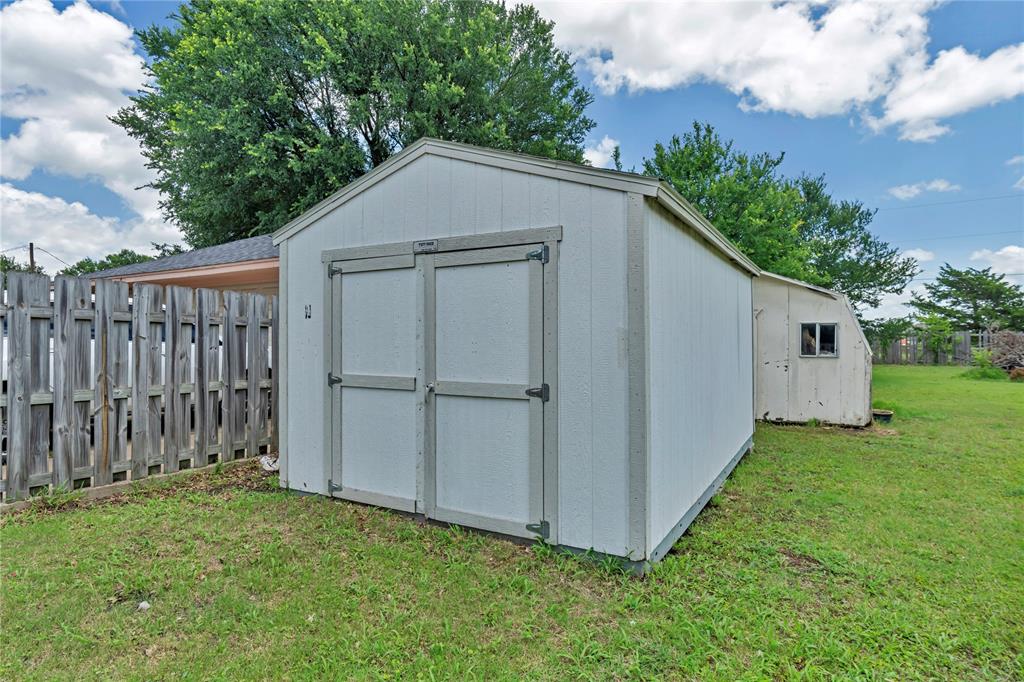 108 Prairie Creek Road Red Oak, TX 75154 - Photo 18 of 19 White storage shed with double doors, wood fencing, and a grassy perimeter