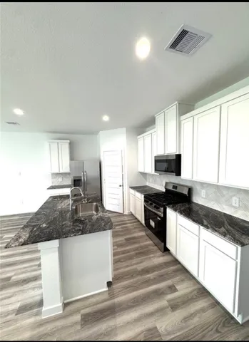 a large kitchen with granite countertop a sink dishwasher a stove and white cabinets with wooden floor