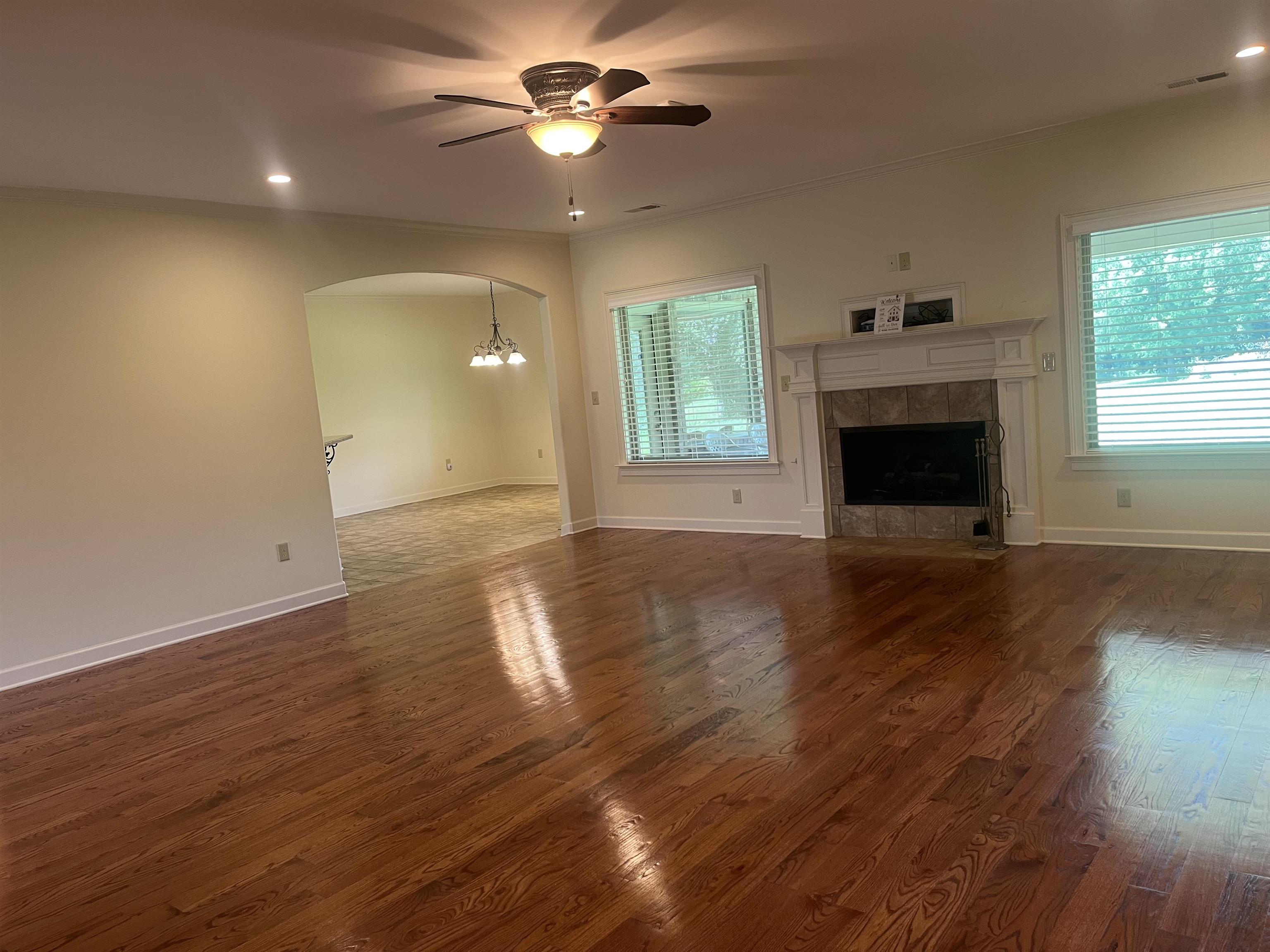 185 Belmont Road Mason, TN 38049 - Photo 14 of 40 Spacious living area featuring wood-finish flooring, a fireplace with a stone surround and white mantel, and multiple windows with blinds