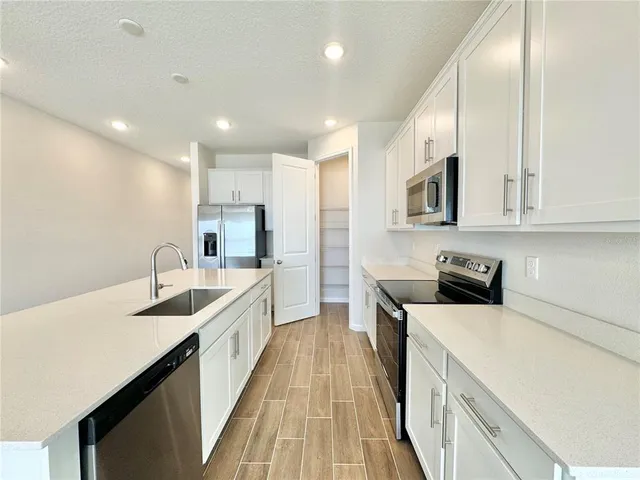 a large kitchen with stainless steel appliances a large counter top a stove a sink a refrigerator white cabinets and wooden floor