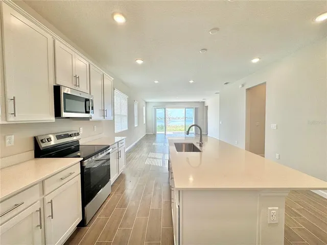 a large kitchen with kitchen island a sink a stove a refrigerator and white cabinets with wooden floor