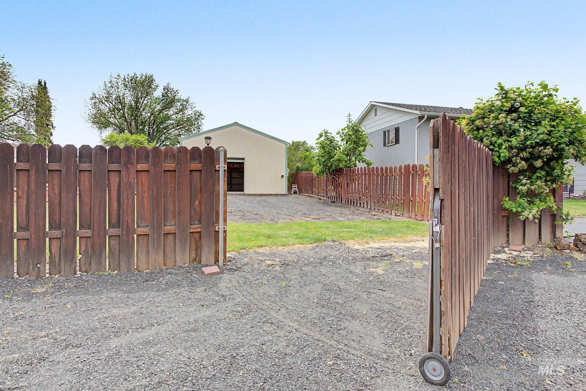 3314 6th Street Lewiston, ID 83501 - Photo 40 of 50 Expansive gravel driveway with a wood-plank privacy fence, leading to a detached structure featuring light-colored siding and a dark roof