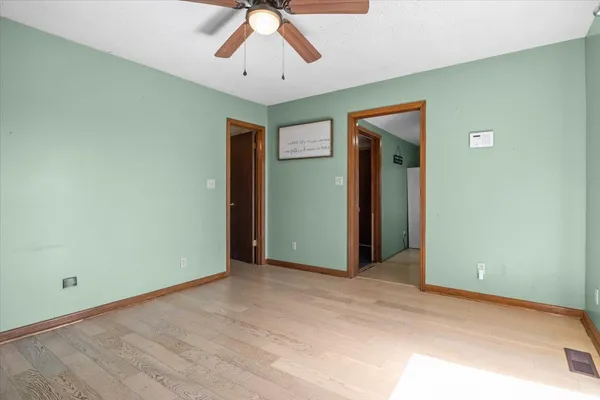 an empty room with chandelier fan and wooden floor