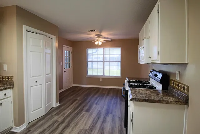 a kitchen with stainless steel appliances granite countertop a stove a sink and white cabinets with wooden floor