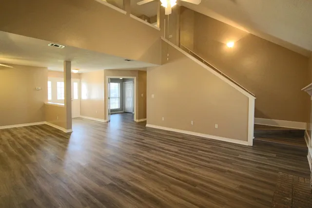 a view of an empty room with wooden floor and a ceiling fan
