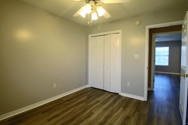 an empty room with wooden floor chandelier fan and windows
