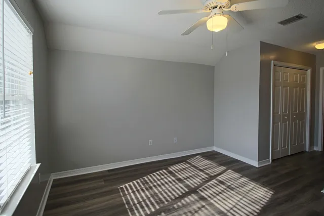 an empty room with wooden floor fan and windows