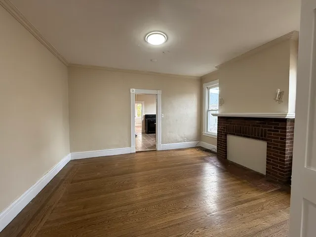 a view of an empty room with wooden floor fireplace and a window