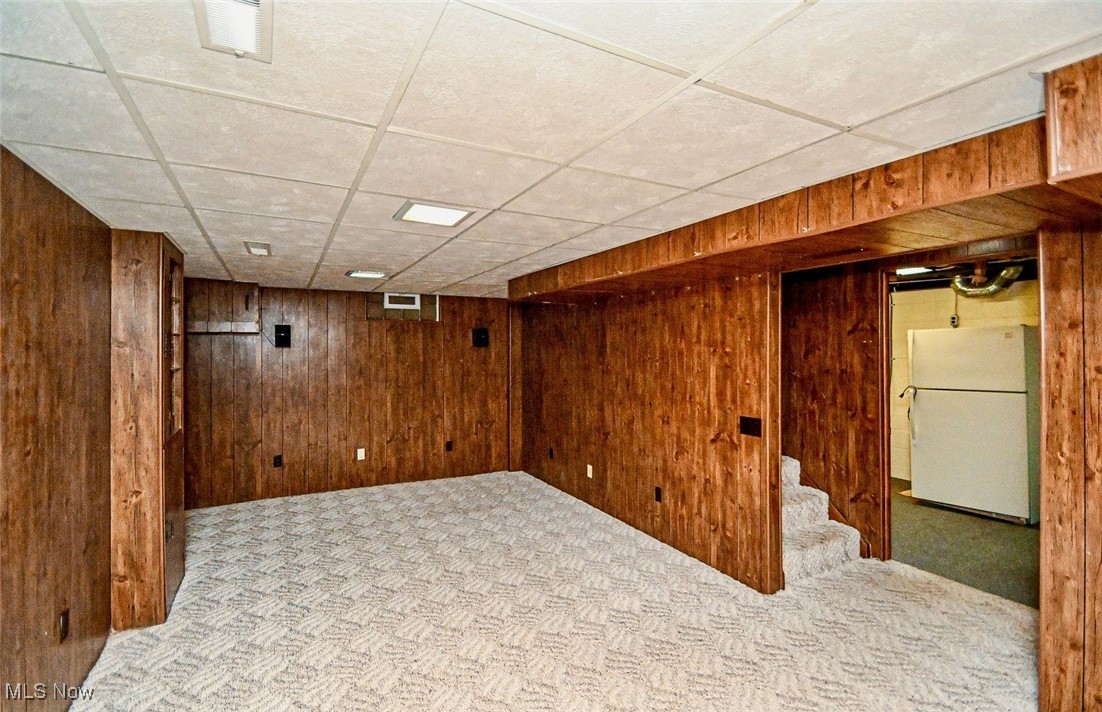 4858 Arbor Road Southwest Canton, OH 44710 - Photo 10 of 31 Basement featuring light colored carpet, wood walls, white fridge, and a paneled ceiling