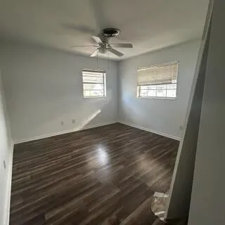 an empty room with wooden floor chandelier fan and windows