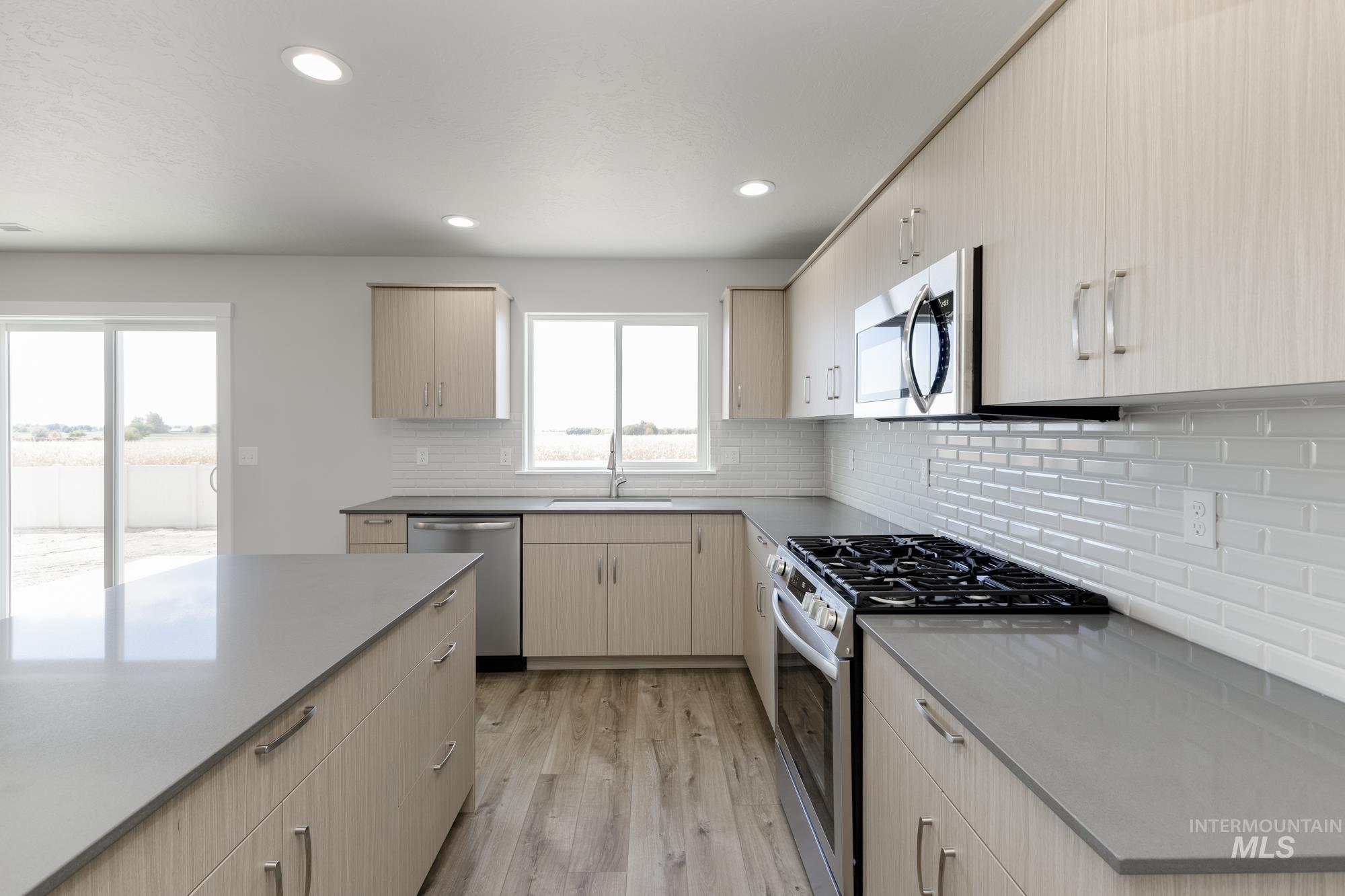 12853 Decatur Street Nampa, ID 83651 - Photo 5 of 24 Kitchen featuring light wood-finish cabinetry, gray countertops, a stainless steel gas range, a coordinating stainless steel microwave, and white subway tile backsplash