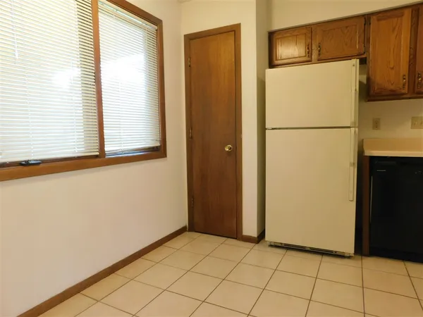 a view of a refrigerator in kitchen and an empty room in wooden floor