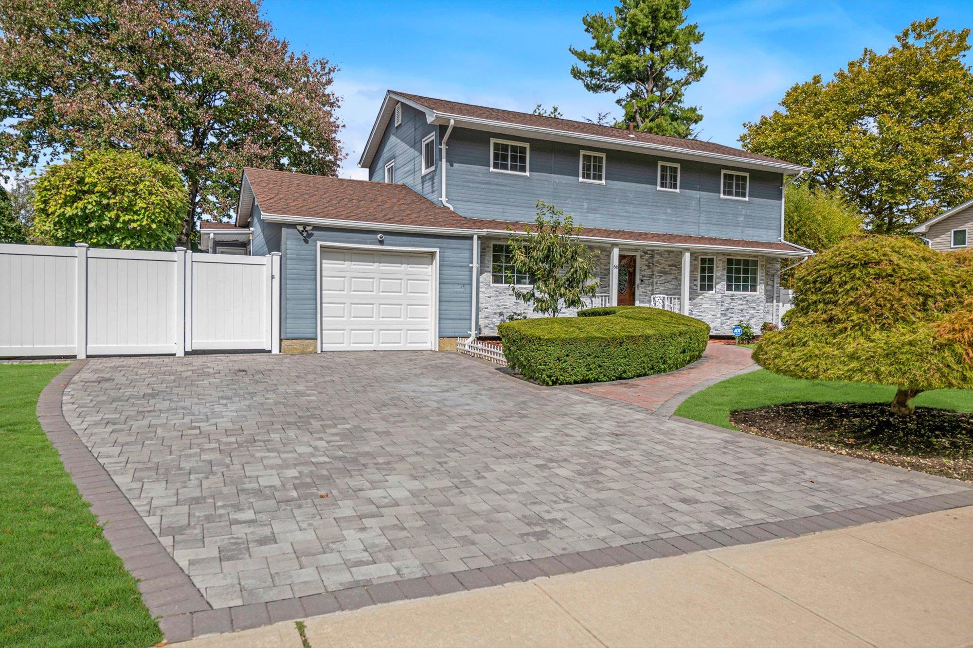 View of front facade featuring fence, decorative driveway, an attached garage, stone siding, and a porch