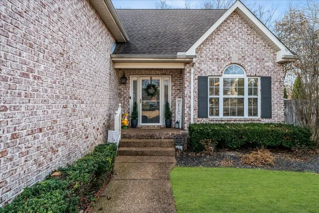 a view of a brick house with a yard plants and large tree