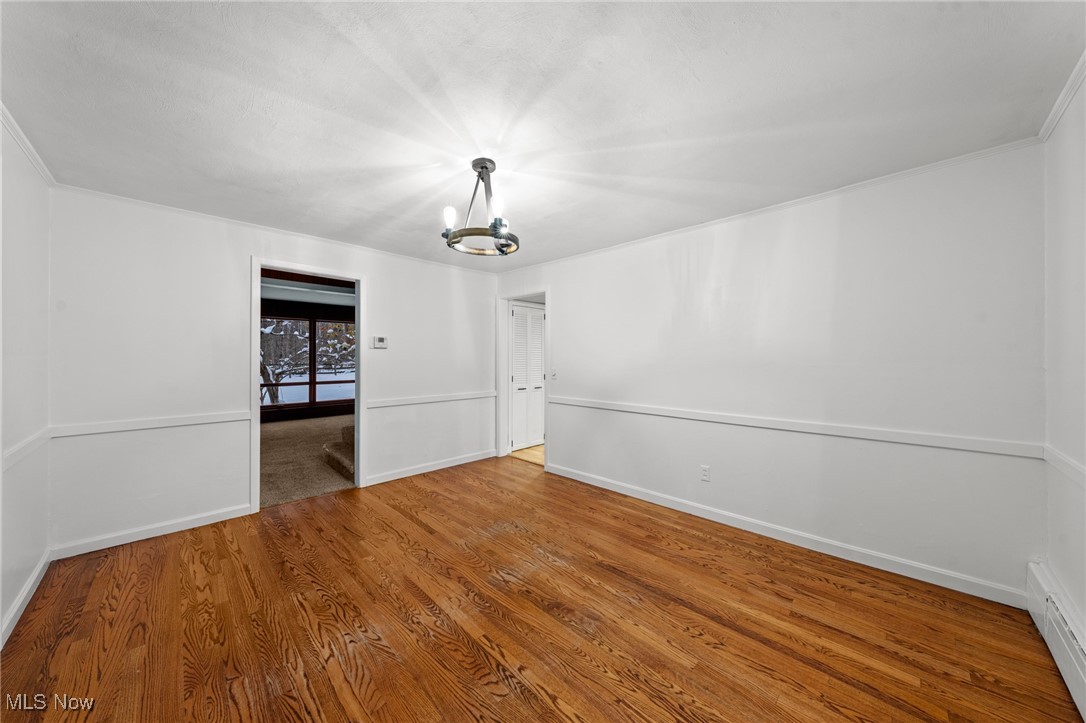 9513 Booth Road Willoughby, OH 44094 - Photo 13 of 45 Spare room with hardwood / wood-style flooring, ornamental molding, a baseboard radiator, and a chandelier