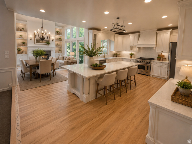 11902 Autumn Ridge Drive East Sandy, UT 84092 - Photo 8 of 20 Open-concept living space featuring wood-finish flooring, a kitchen with white cabinetry and a large island with seating, a dining area, and a living room with a fireplace and built-in shelving AI-staged or enhanced
