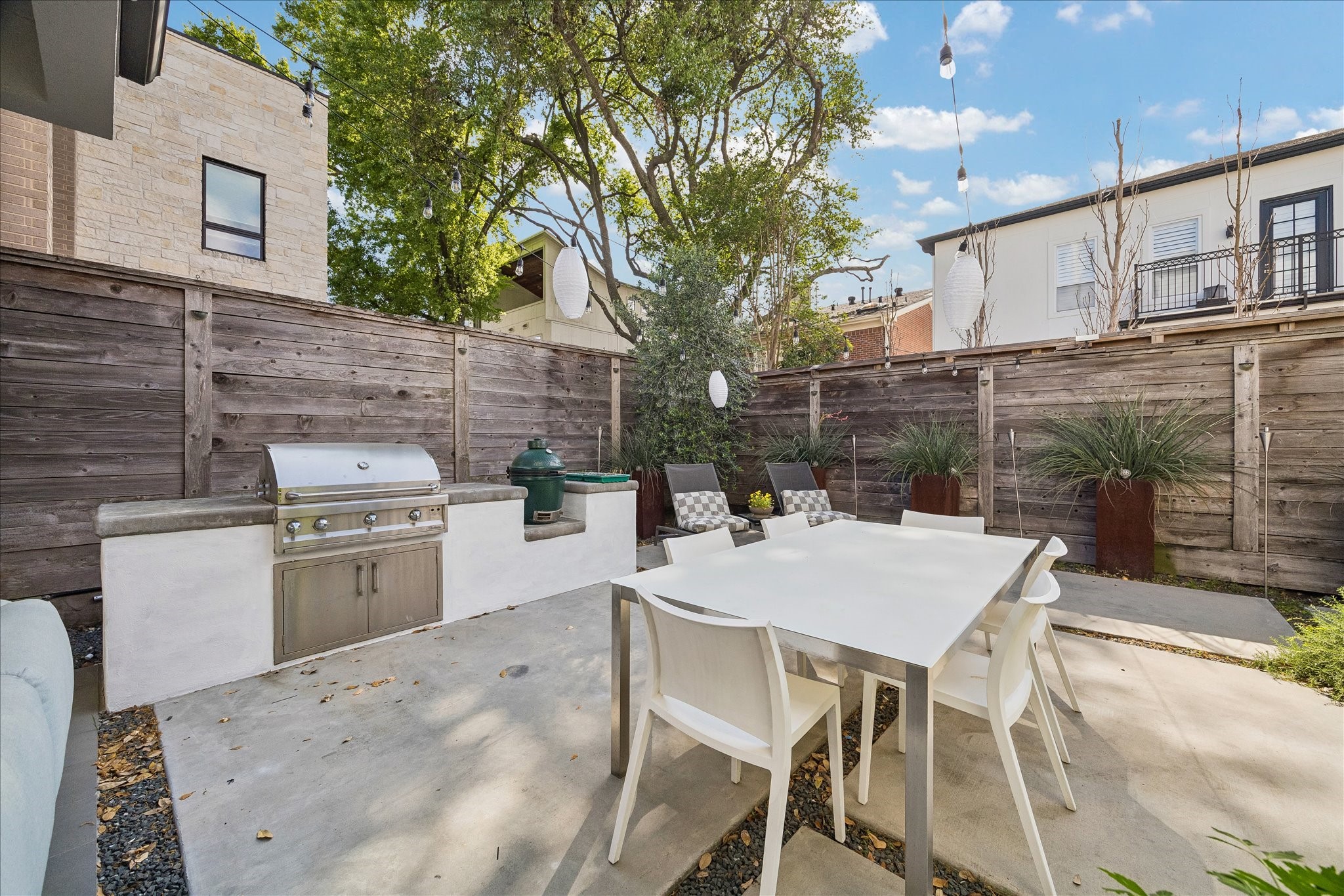 2014 Park Street Houston, TX 77019 - Photo 13 of 40 This photo showcases a modern outdoor patio with a built-in grill, dining area, and seating. Surrounded by a wooden privacy fence and lush greenery, it's perfect for entertaining and relaxing.