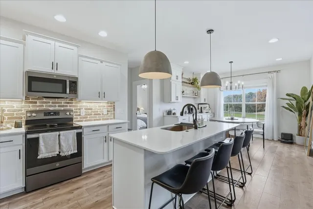 a kitchen with stainless steel appliances a stove a sink a microwave a dining table and chairs with wooden floor