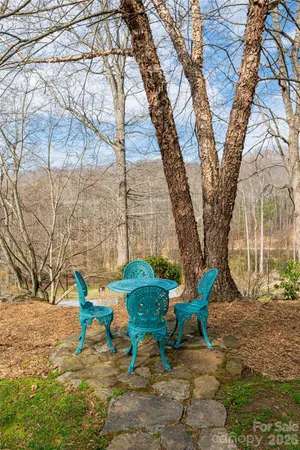 a backyard of a house with table and chairs under a large tree