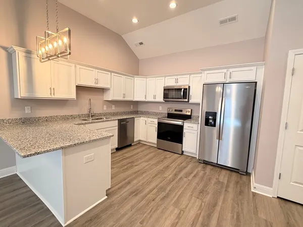 a kitchen with stainless steel appliances granite countertop a refrigerator a sink dishwasher a stove and white countertops with wooden floor