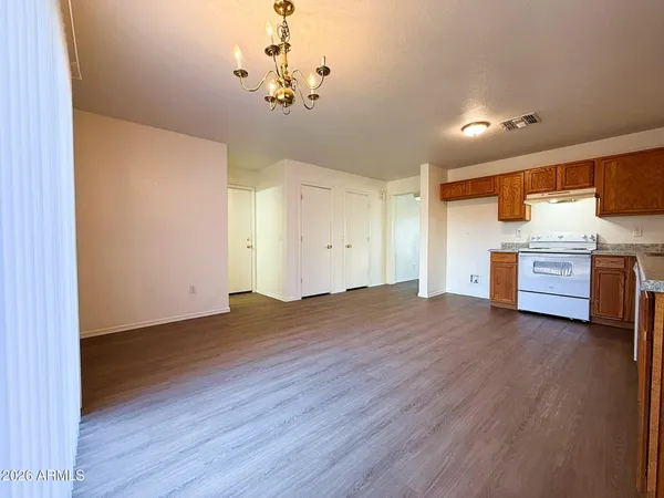 a view of an empty room and kitchen with wooden floor