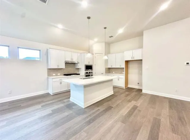 a view of kitchen with granite countertop refrigerator oven a sink and white cabinets with wooden floor
