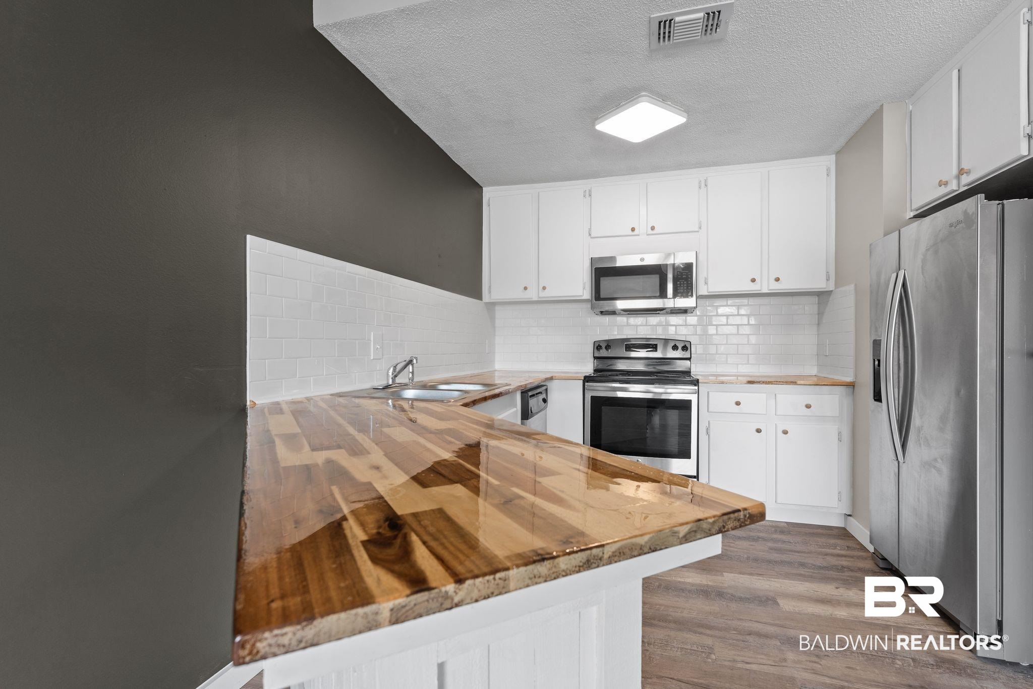 128 West Satsuma Avenue, Unit 128 Foley, AL 36535 - Photo 13 of 41 Kitchen featuring butcher block counters, stainless steel appliances, white cabinetry, dark wood finished floors, and a textured ceiling