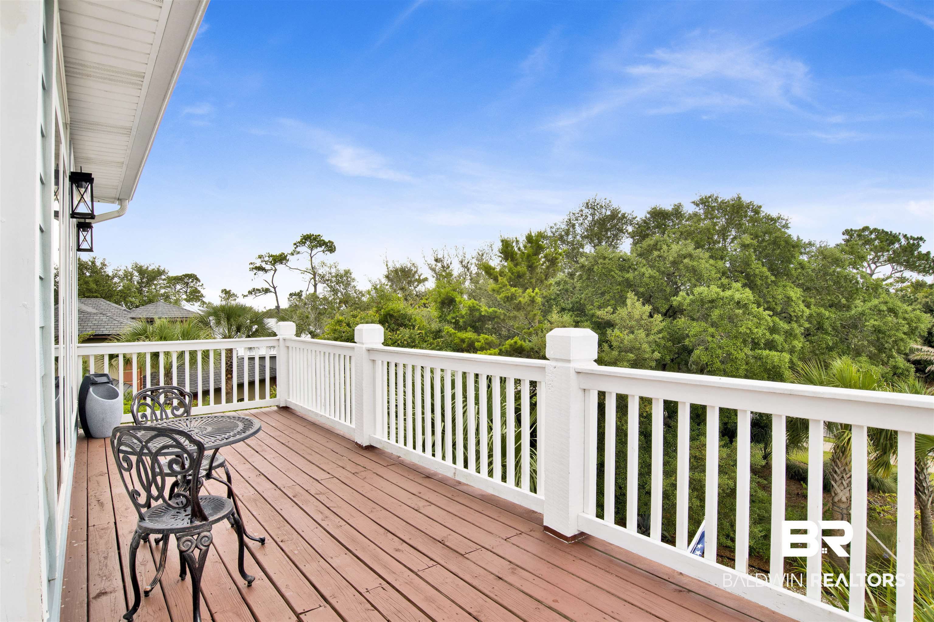 30351 River Road Orange Beach, AL 36561 - Photo 19 of 44 Wood-finish deck with white balustrade railing, featuring black exterior sconces, and surrounding mature trees