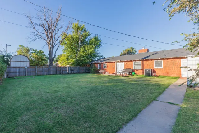 a view of a backyard with plants and large trees with wooden fence