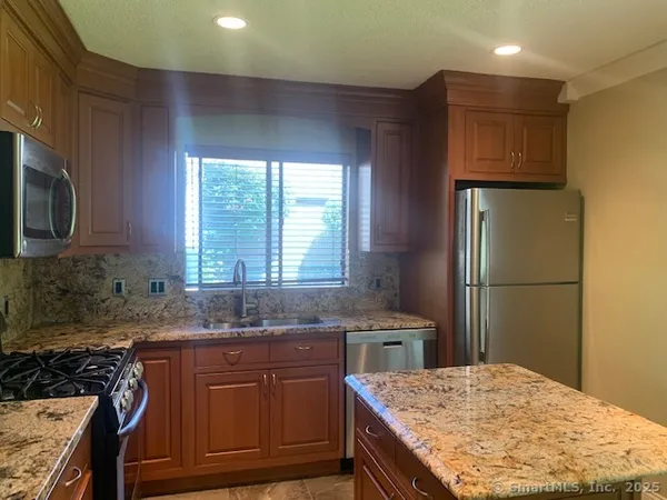 a kitchen with kitchen island granite countertop wooden cabinets a sink a stove a refrigerator and island