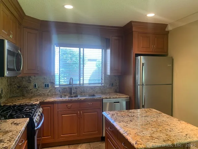 a kitchen with kitchen island granite countertop wooden cabinets a sink a stove a refrigerator and island