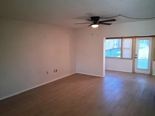 an empty room with wooden floor fan and windows